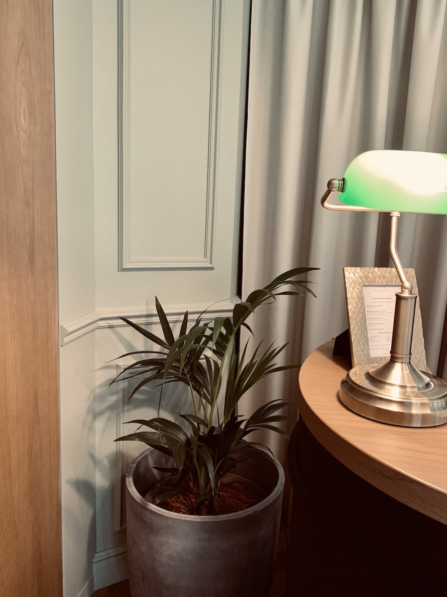 Coin lecture classique avec lampe banquier verte, palmier d'intérieur en pot gris, et boiserie vert pâle élégante. Table en chêne.