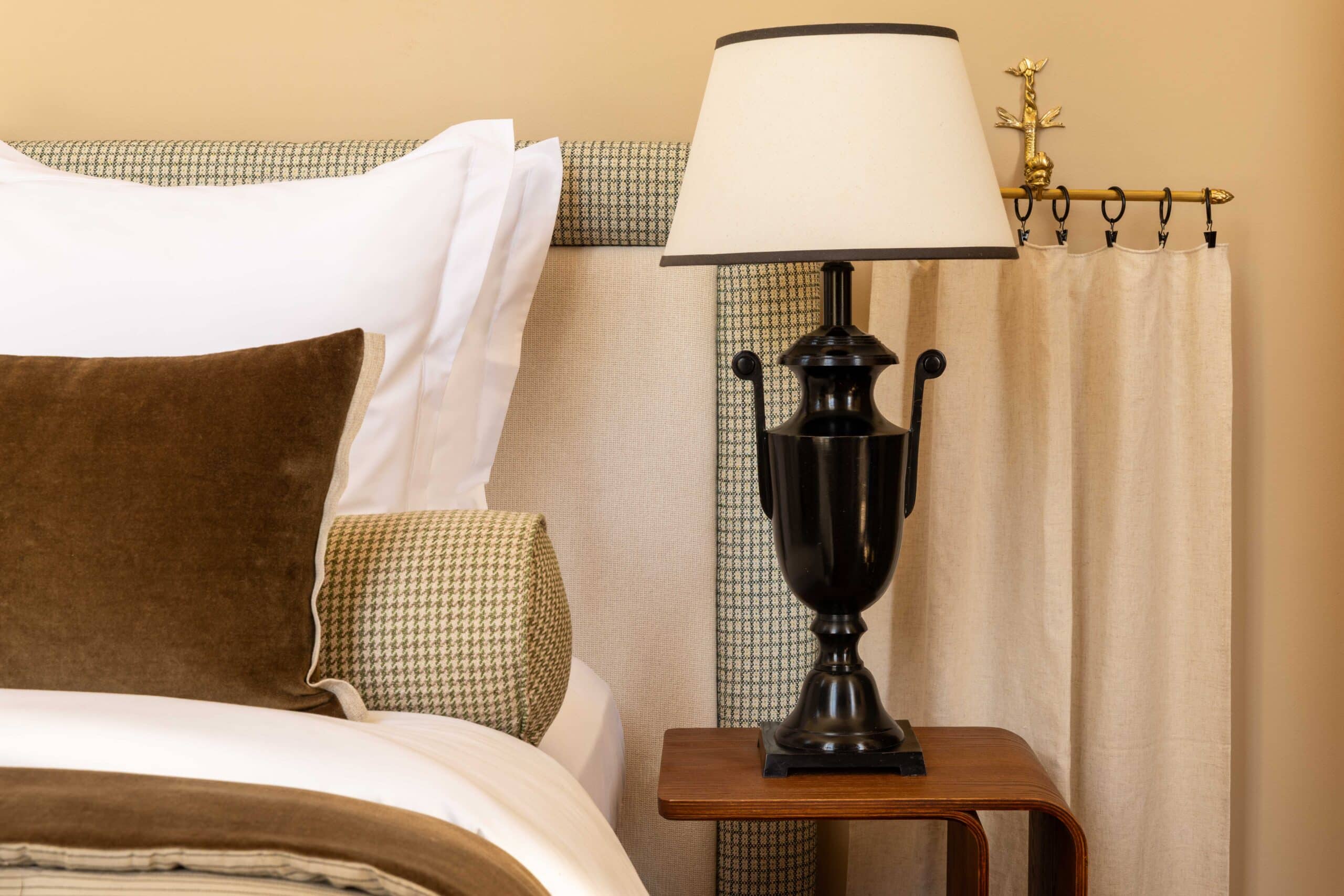 Tête de lit en tweed vert et beige, coussins velours marron. Lampe urne noire sur table de chevet en bois courbé.