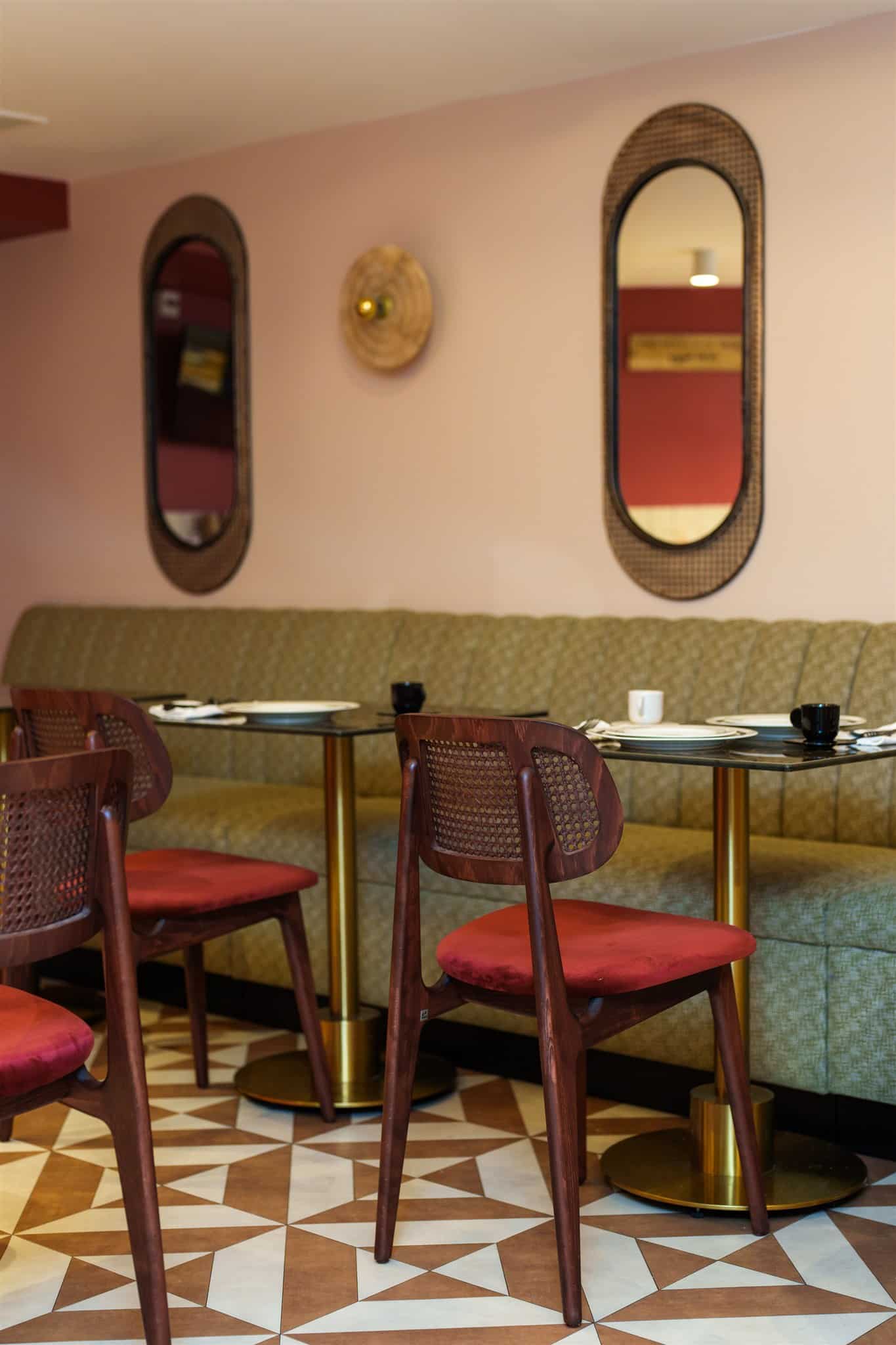 Design intérieur rétro chic : chaises en bois foncé, assise velours rouge, banquette vert olive. Murs rose pâle, miroirs en rotin.