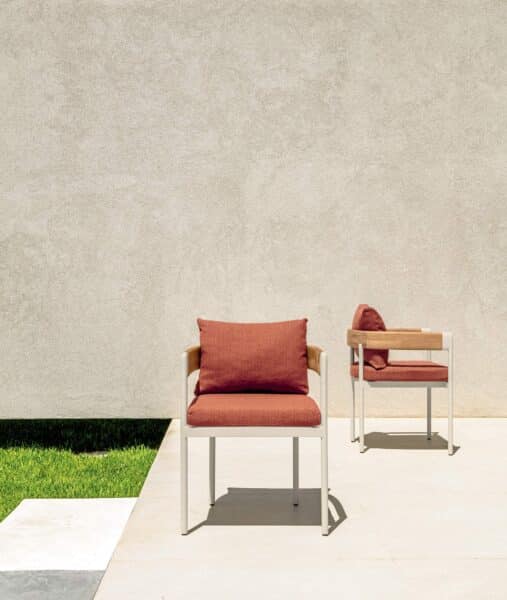 Deux chaises d'extérieur design. Cadre métal blanc, accoudoirs bois et coussins terracotta sur une terrasse ensoleillée minimaliste.