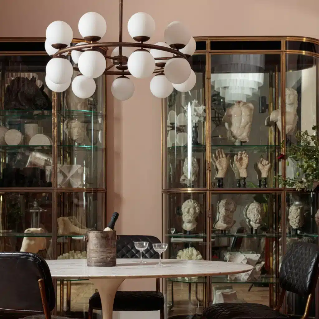 Salle à manger sophistiquée : lustre moderne, table en marbre, chaises matelassées. Vitrines murales remplies de sculptures classiques.